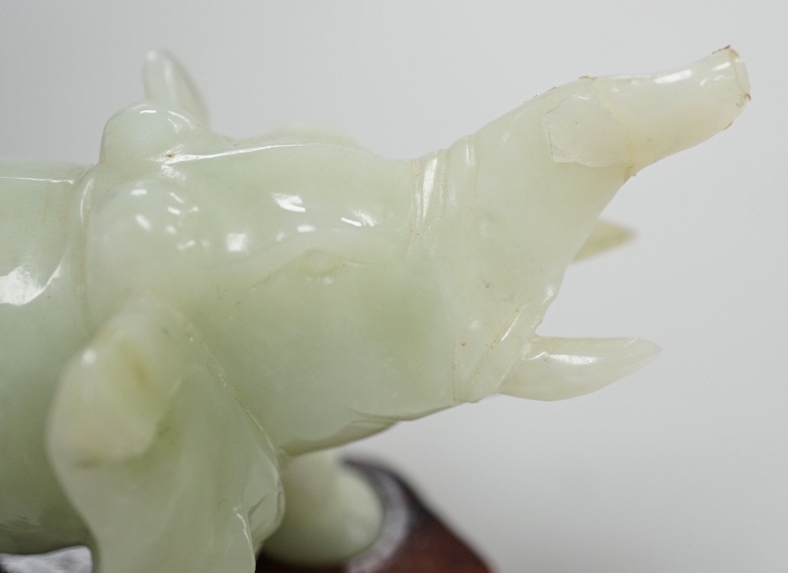 A Chinese bowenite jade elephant on hard wood stand, 11cm tall